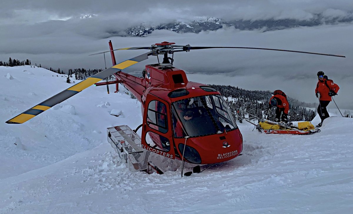 Doug and ski patroller beside a helicopter in the snow, awaiting patient load